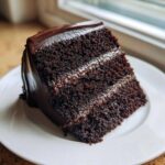 Close-up of a decadent slice of moist chocolate cake layered with dark chocolate frosting.