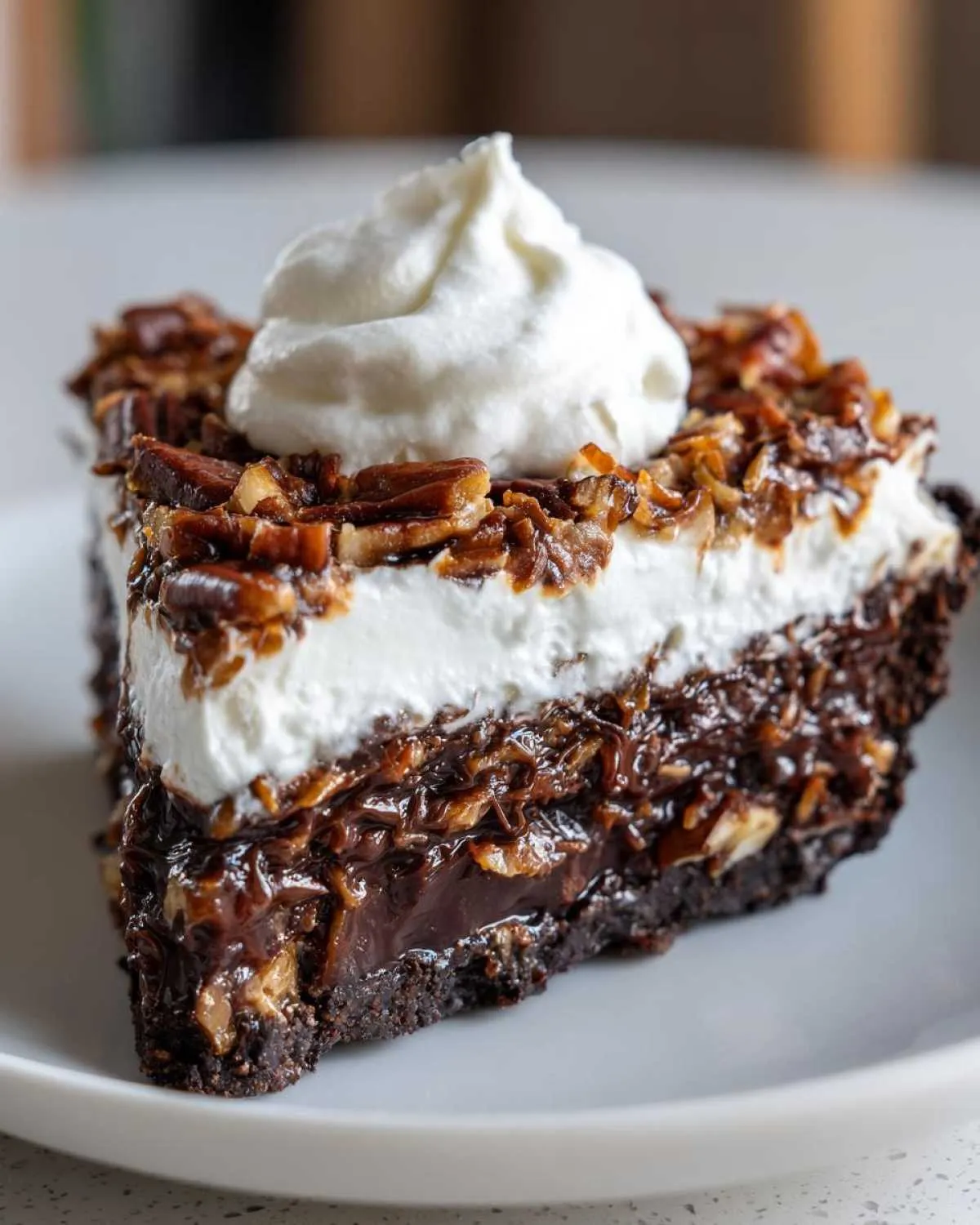 A rich, layered slice of no-bake german chocolate pie topped with coconut-pecan filling and whipped cream.