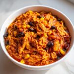 Close-up of a white bowl filled with thick, shredded slow cooker buffalo chicken chili featuring black beans and corn.