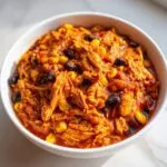Close-up of a white bowl filled with thick, shredded slow cooker buffalo chicken chili featuring black beans and corn.
