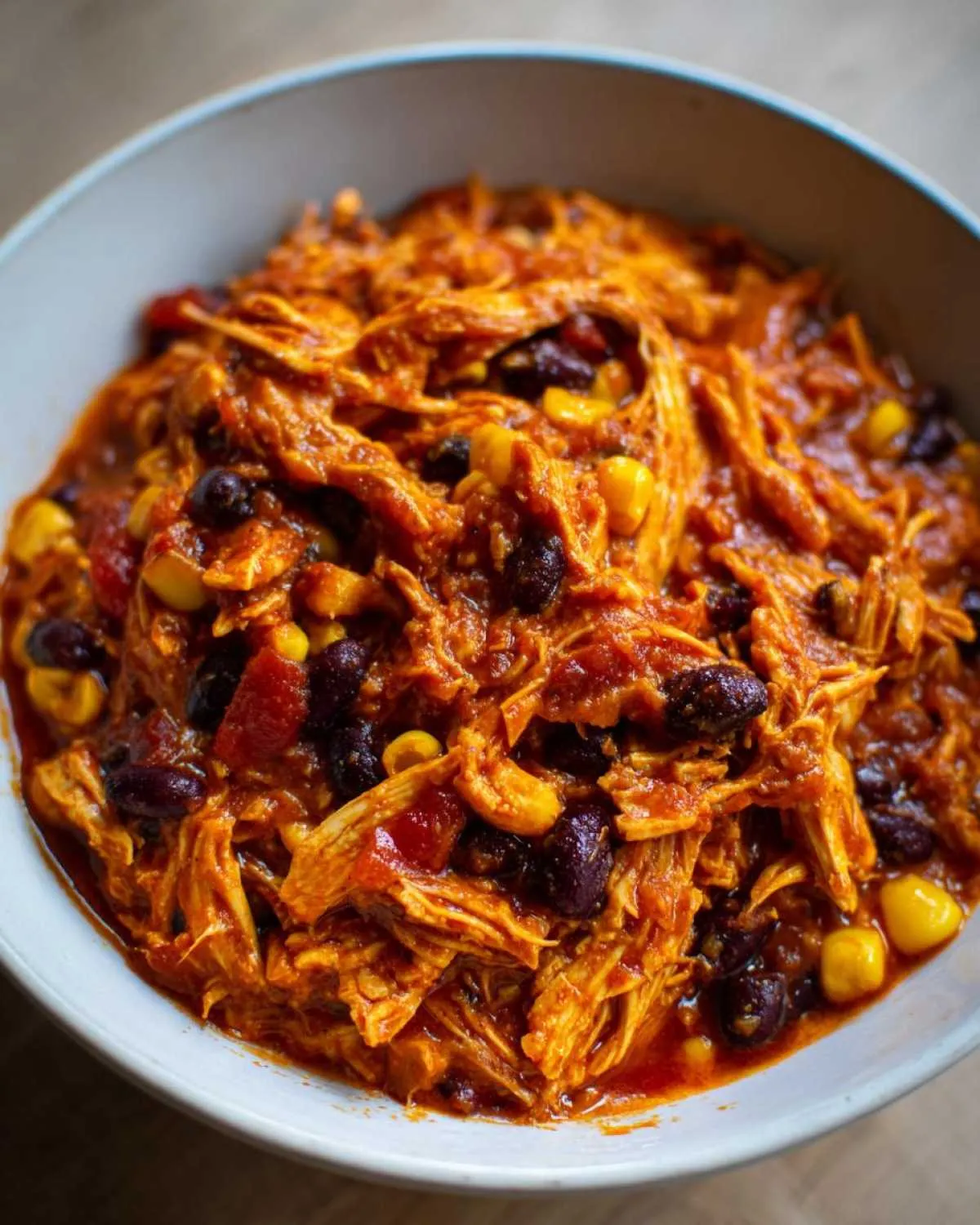 Close-up of shredded chicken in a rich, orange-red sauce with black beans and corn, representing slow cooker buffalo chicken chili.