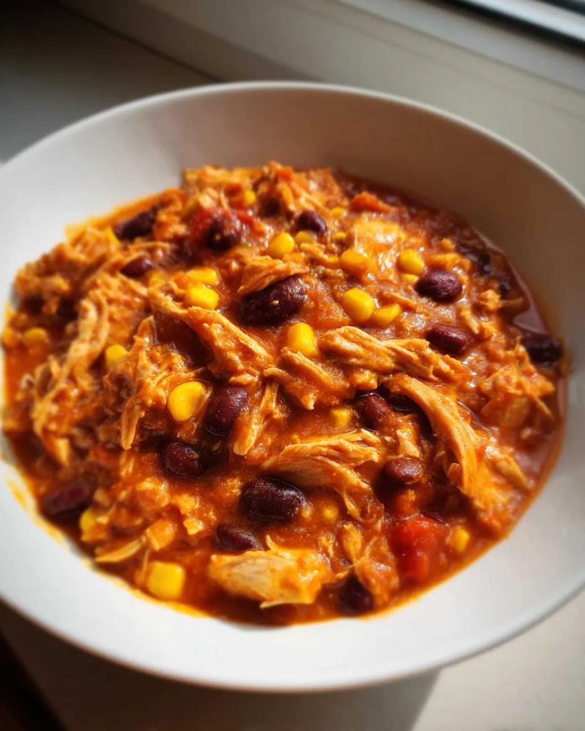 Close-up of a white bowl filled with saucy slow cooker buffalo chicken chili featuring shredded chicken, kidney beans, and corn.