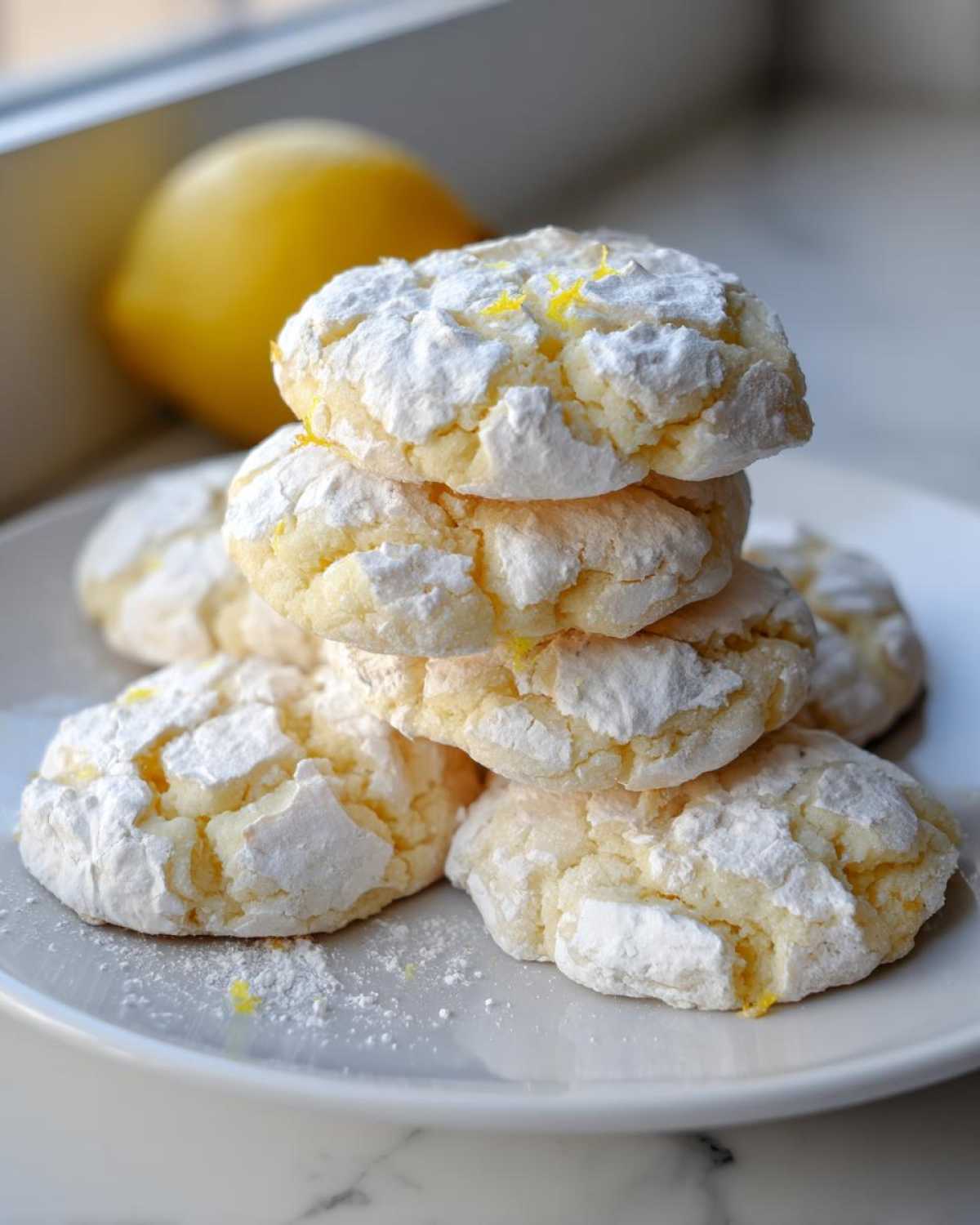 A stack of soft lemon crinkle cookies coated in powdered sugar, with a fresh lemon in the background.
