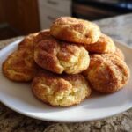 A stack of freshly baked, soft snickerdoodle cookies coated in cinnamon sugar, resting on a white plate.