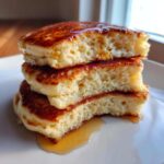 Close-up of a stack of three fluffy sourdough discard pancakes, drizzled with syrup.