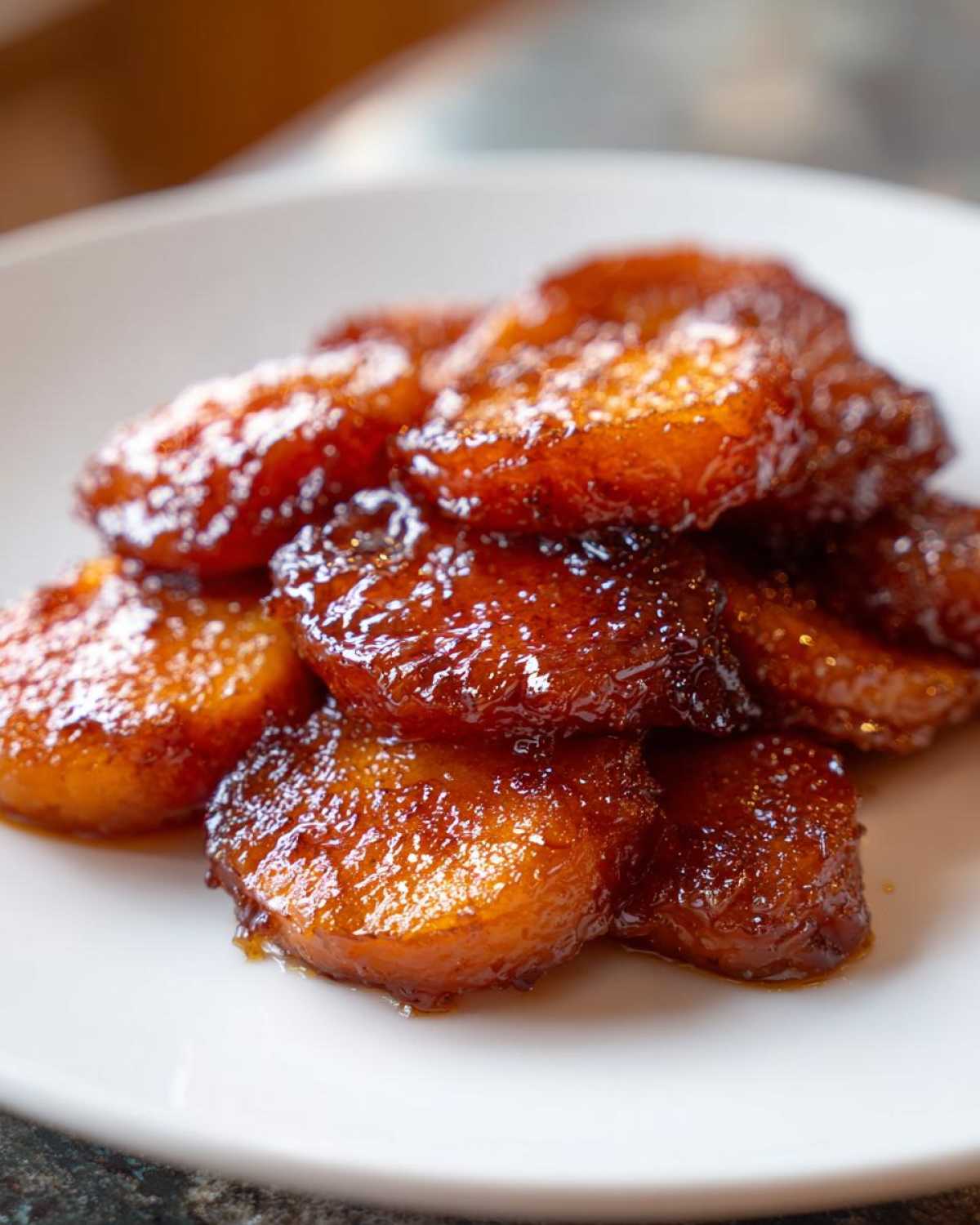 A close-up of sweet, glistening southern candied yams piled on a white plate.