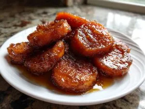 A serving of thick, glazed southern candied yams piled high on a white plate, glistening with syrup.