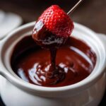 A fresh strawberry being dipped into a white pot of warm, melted chocolate fondue.