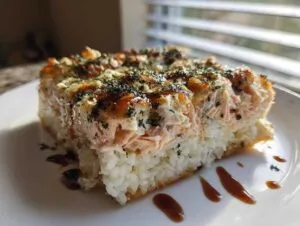 A thick, square slice of baked salmon sushi bake casserole served on a white plate.