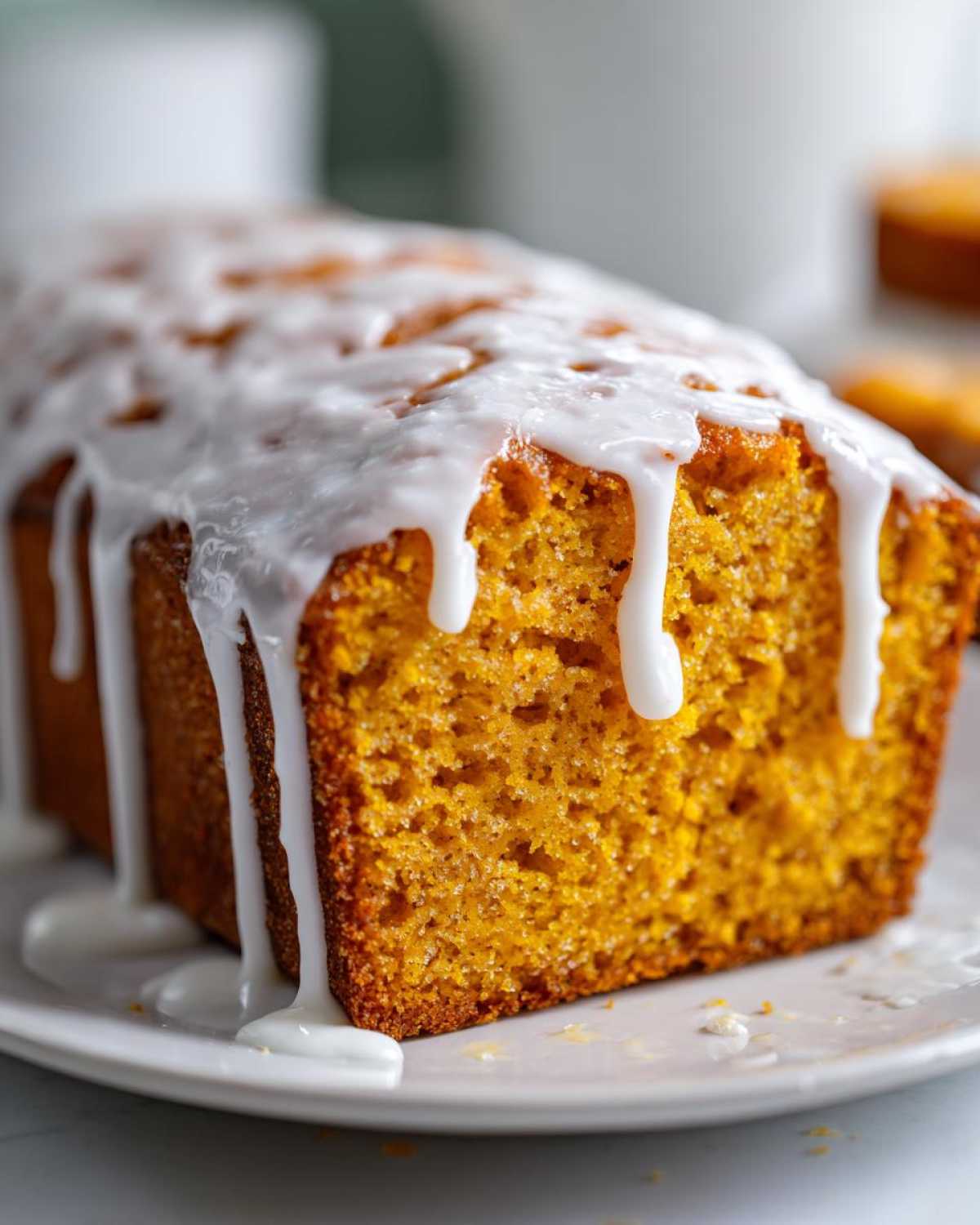 Close-up of a slice of vibrant orange sweet potato pound cake topped with thick white vanilla glaze drips.