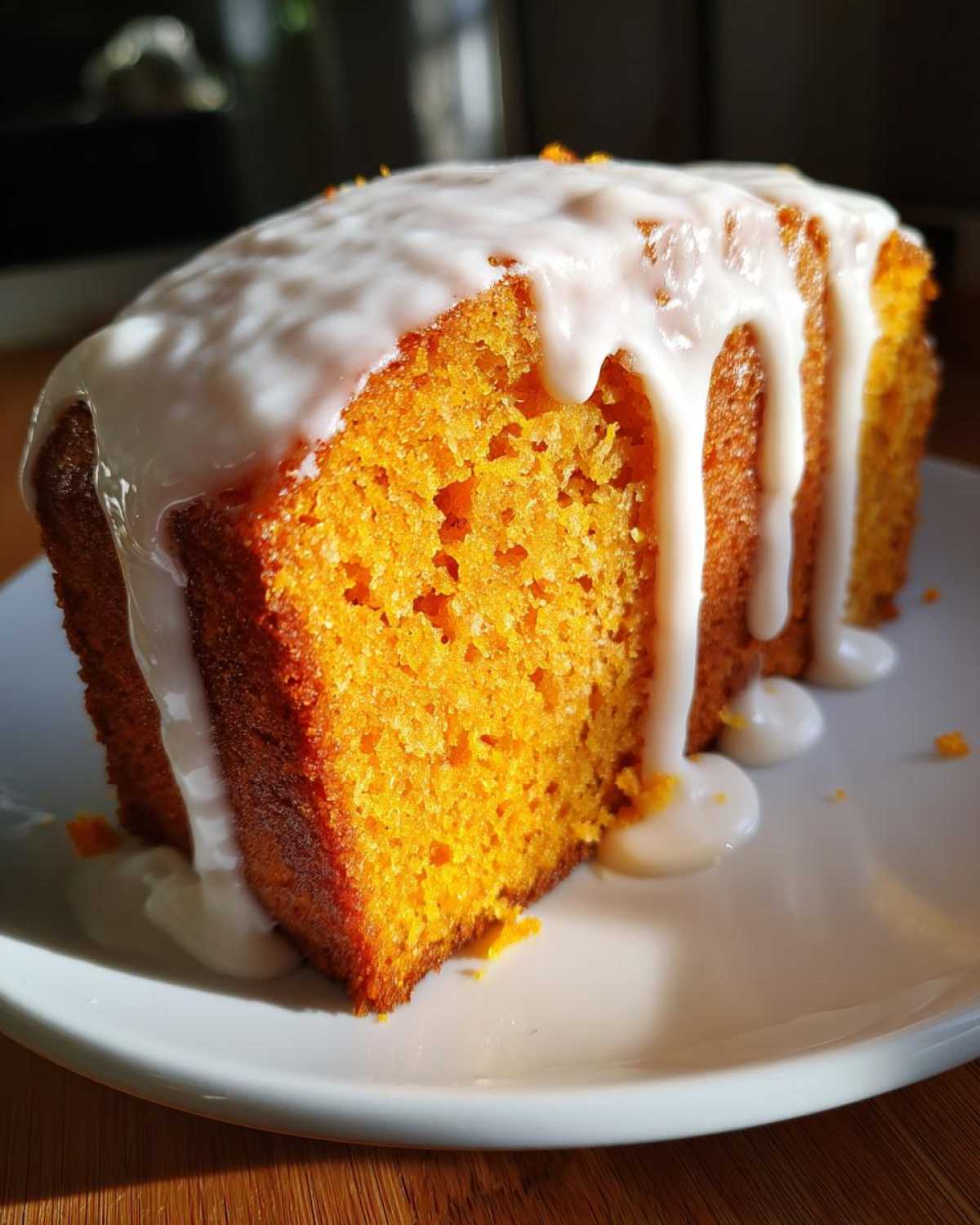 A moist slice of bright orange sweet potato pound cake topped with thick white vanilla glaze dripping down the sides.