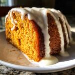 A close-up of a moist slice of sweet potato pound cake topped with thick white glaze.