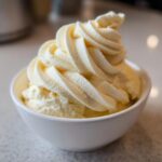 A close-up of creamy, soft-serve style banana ice cream swirled high in a small white bowl.