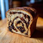 Close-up of a freshly baked loaf of raisin bread showing a beautiful cinnamon swirl packed with dark raisins.