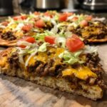 A thick slice of taco pizza showing seasoned ground beef, melted cheddar cheese, lettuce, and diced tomatoes on a thick crust.