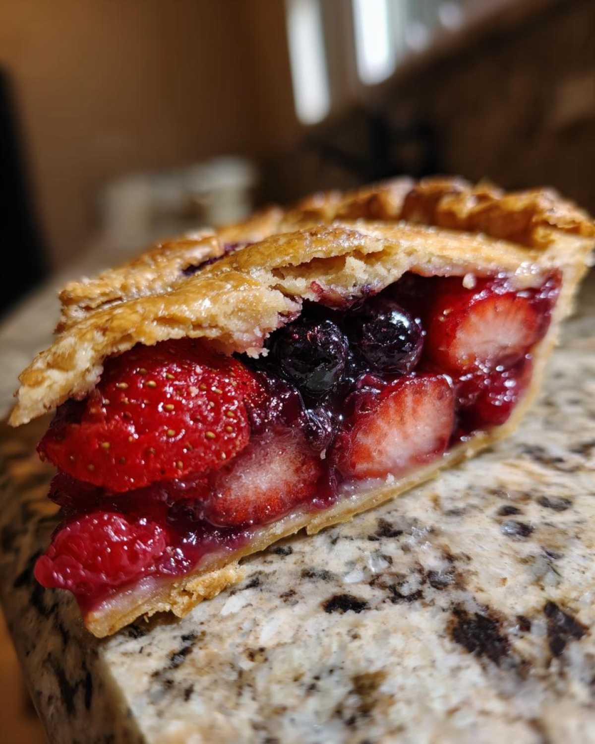 Close-up of a slice of triple berry pie showing strawberries and blueberries in a juicy filling.