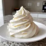 A tall, perfectly piped swirl of creamy white vanilla buttercream frosting on a small white plate.