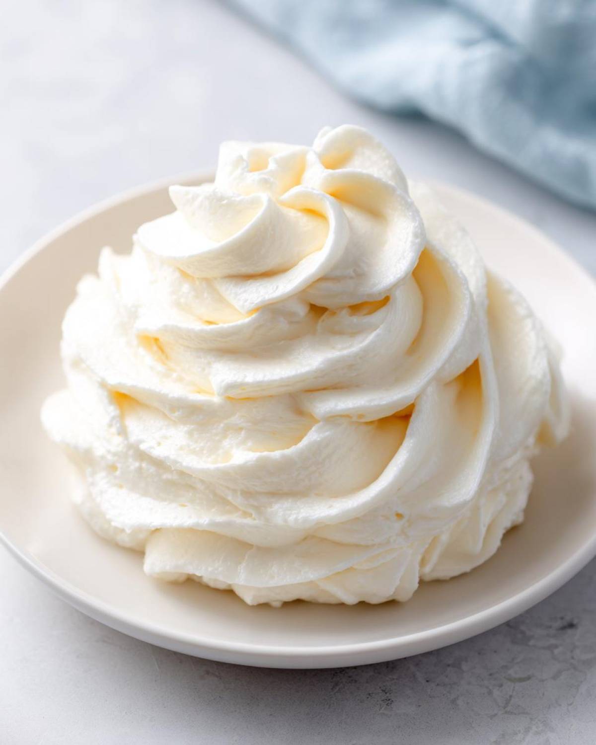 A beautiful, tall swirl of light, creamy vanilla buttercream frosting piped onto a small white plate.
