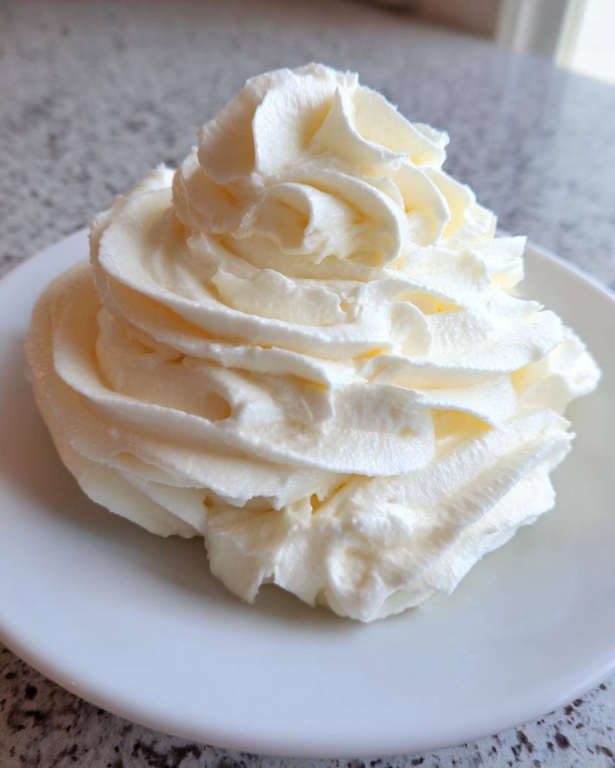 A beautiful, tall swirl of light yellow vanilla buttercream frosting piped onto a small white plate.