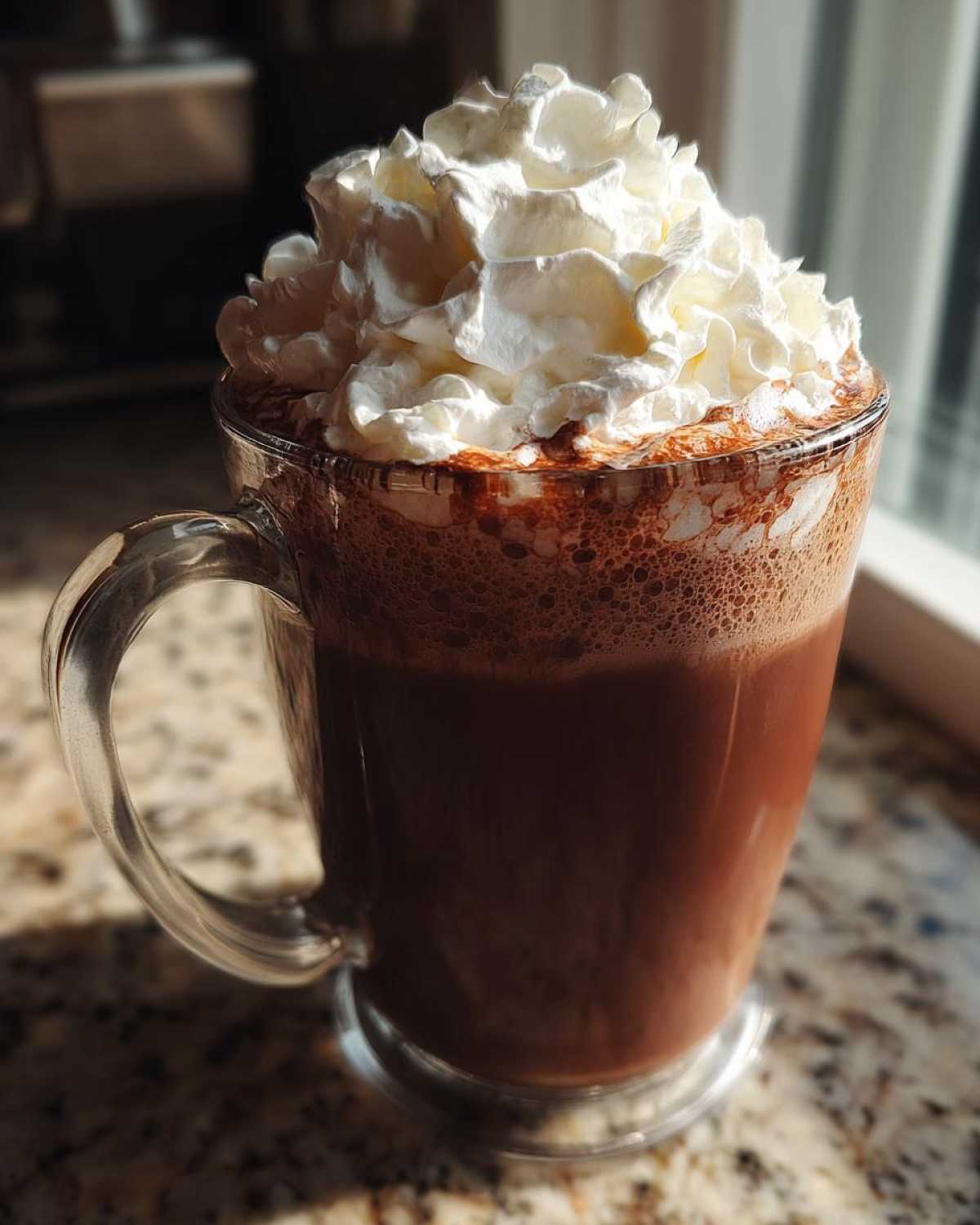 A tall glass mug filled with rich, dark whipped hot chocolate topped with a generous swirl of whipped cream.