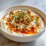 A bowl of creamy whipped ricotta dip topped with hot honey, chopped walnuts, and fresh rosemary sprigs.