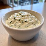 Close-up of creamy, homemade tartar sauce mixed with green herbs and relish, served in a small white bowl.