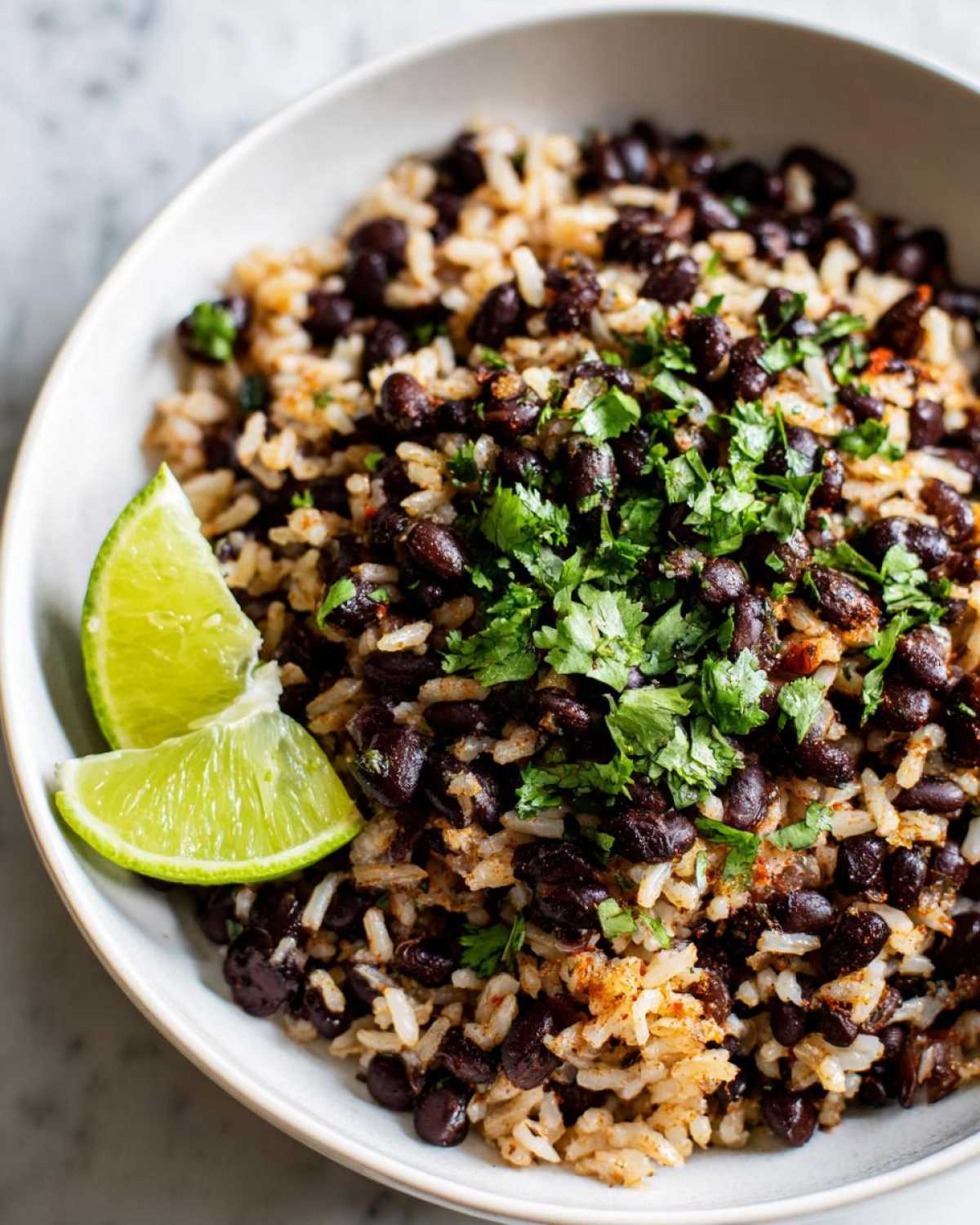 A close-up of a bowl of seasoned beans and rice topped with fresh cilantro and lime wedges, showcasing the beans and rice dish.