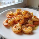 A close-up of perfectly cooked, seasoned air fryer frozen shrimp piled on a white plate.