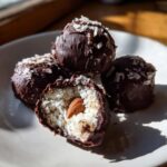 A close-up of homemade almond joy truffles, one cut open to show the coconut filling and whole almond center.