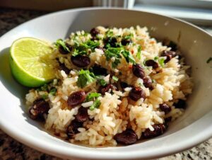Close-up of a white bowl filled with seasoned rice and black beans, topped with cilantro, served with a lime wedge for the amazing beans and rice.