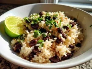 Close-up of a white bowl filled with seasoned rice and black beans, topped with cilantro, served with a lime wedge for the amazing beans and rice.