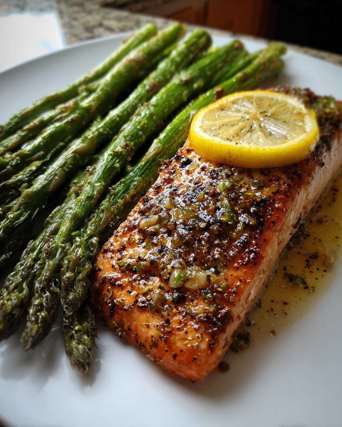 Close-up of a perfectly cooked salmon recipe fillet topped with lemon and herbs, served with roasted asparagus.