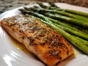 Close-up of a perfectly cooked salmon recipe fillet seasoned with herbs, served alongside bright green asparagus.