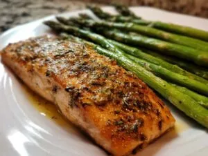 Close-up of a perfectly cooked salmon recipe fillet seasoned with herbs, served alongside bright green asparagus.