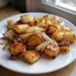 A white plate piled high with golden brown, crispy fried potatoes mixed with sautéed onions.