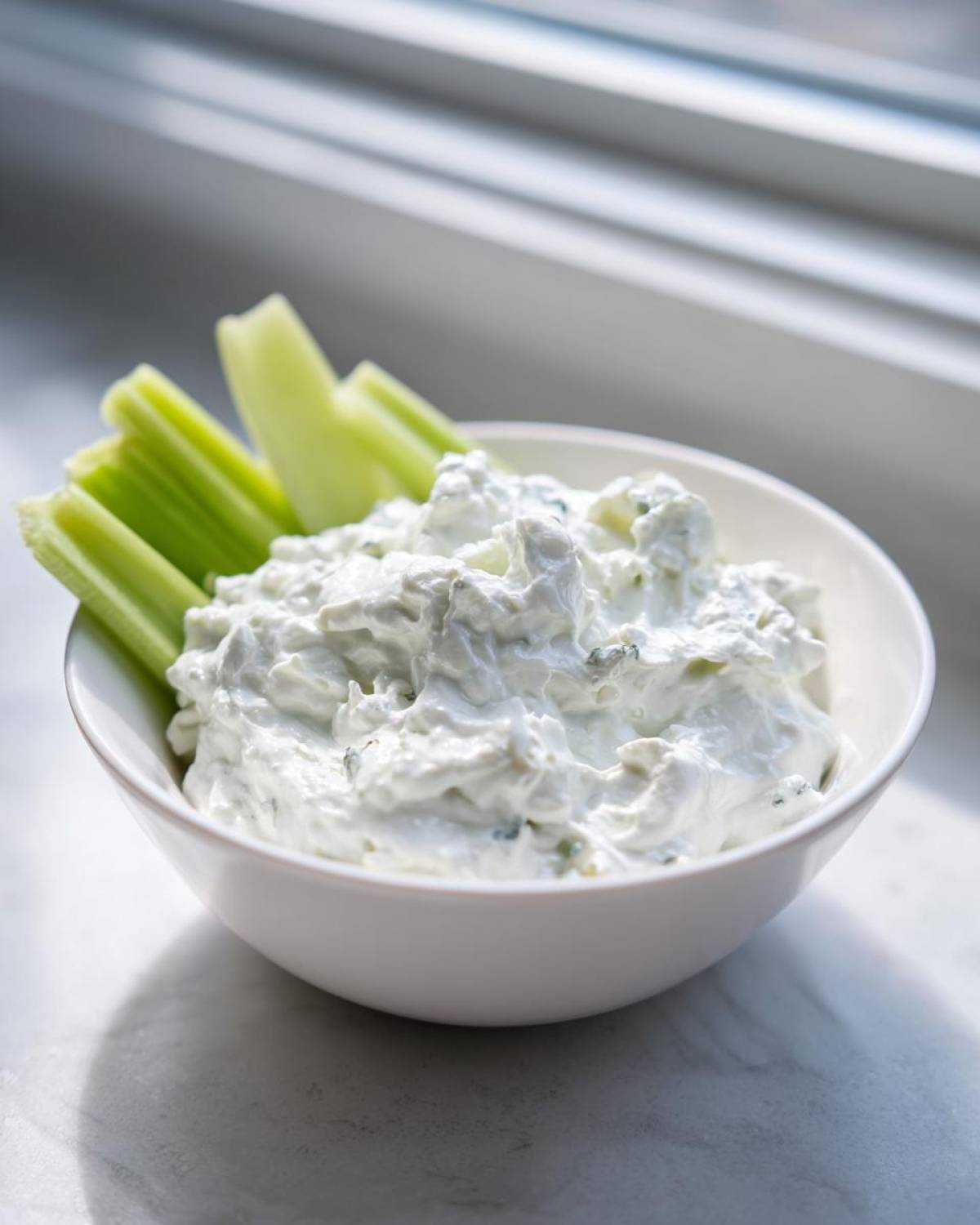 A white bowl filled with creamy blue cheese dip served with crisp celery sticks.