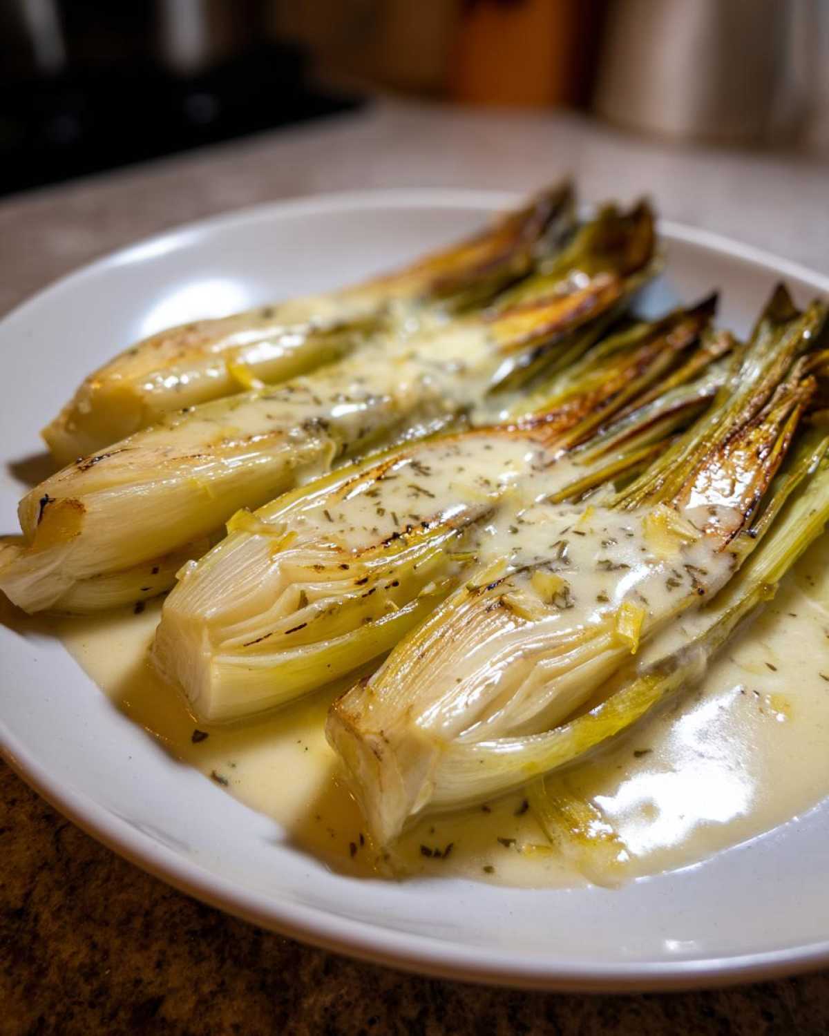 Close-up of tender braised leeks served on a white plate, generously covered in a creamy herb sauce.