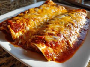 Close-up of two baked cheese enchiladas covered in melted cheddar and Monterey Jack cheese and red sauce.
