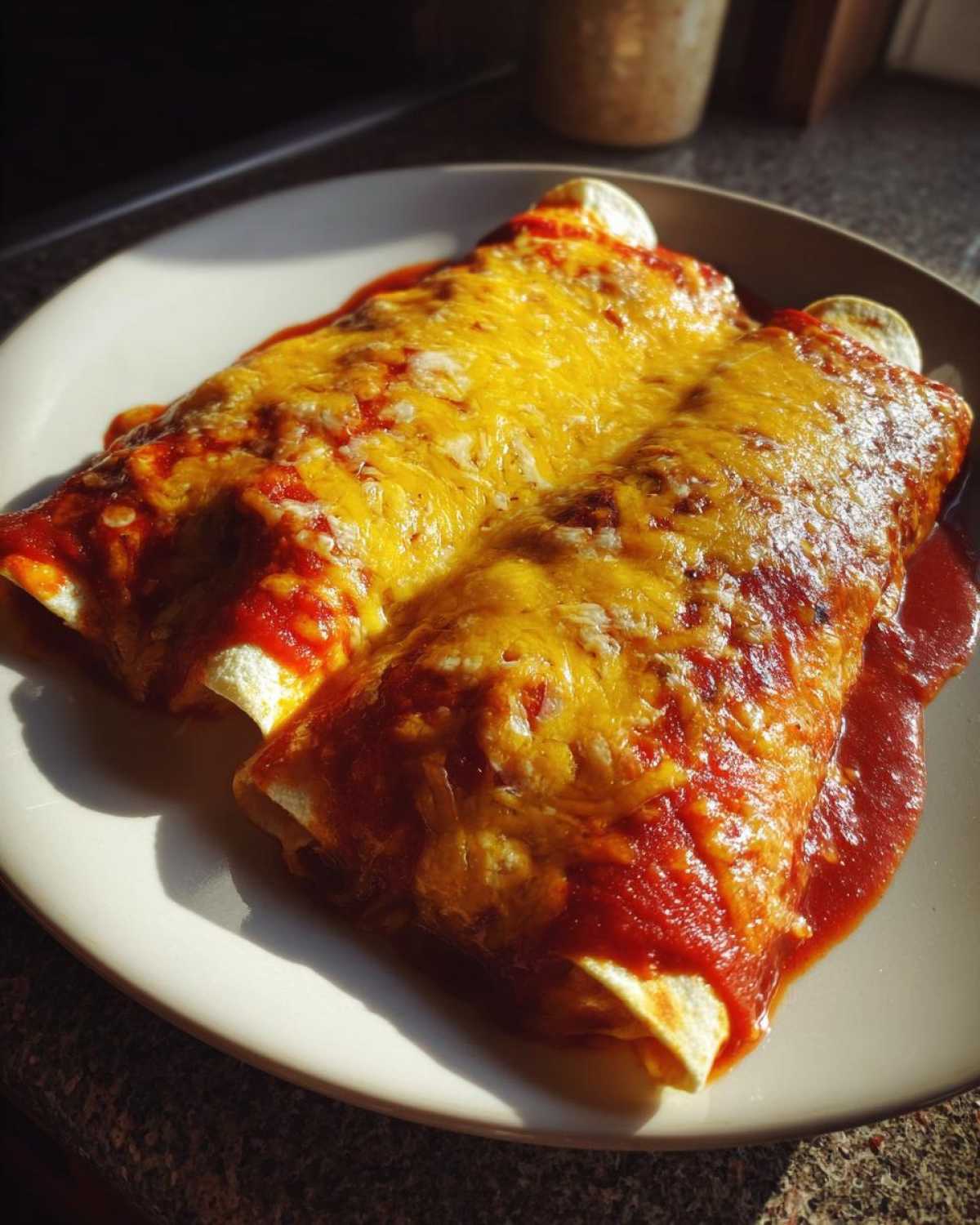 Two delicious cheese enchiladas covered in red sauce and melted cheddar cheese, served on a white plate.
