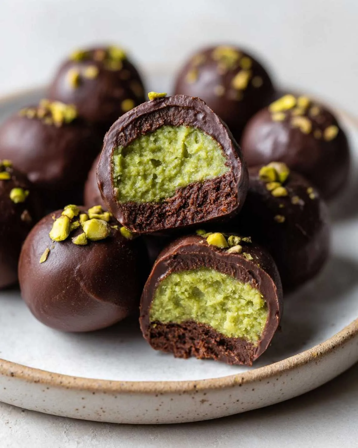 Close-up of amazing dubai chocolate balls cut in half, revealing a bright green pistachio filling over a dark chocolate base.