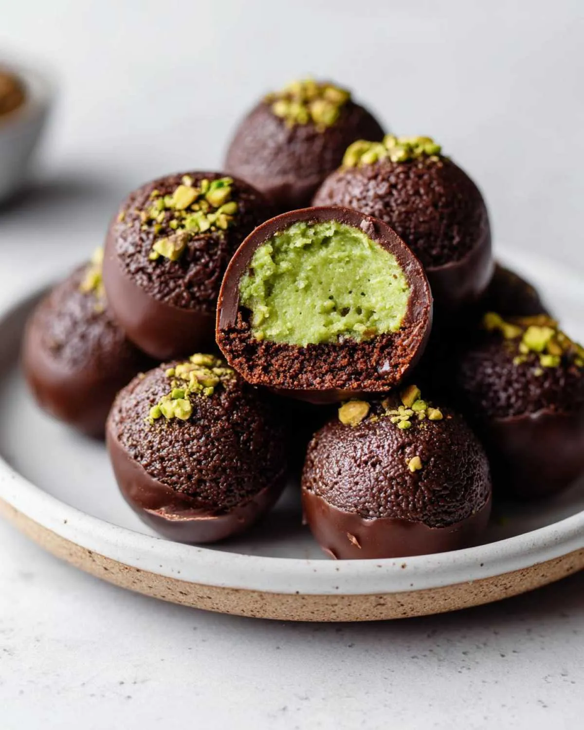 Close-up of amazing dubai chocolate balls stacked, one cut open revealing a bright green pistachio filling inside a chocolate shell.
