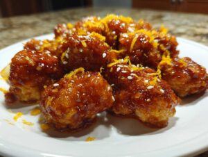 Close-up of crispy, glazed pieces of orange chicken recipe garnished with sesame seeds and bright orange zest.