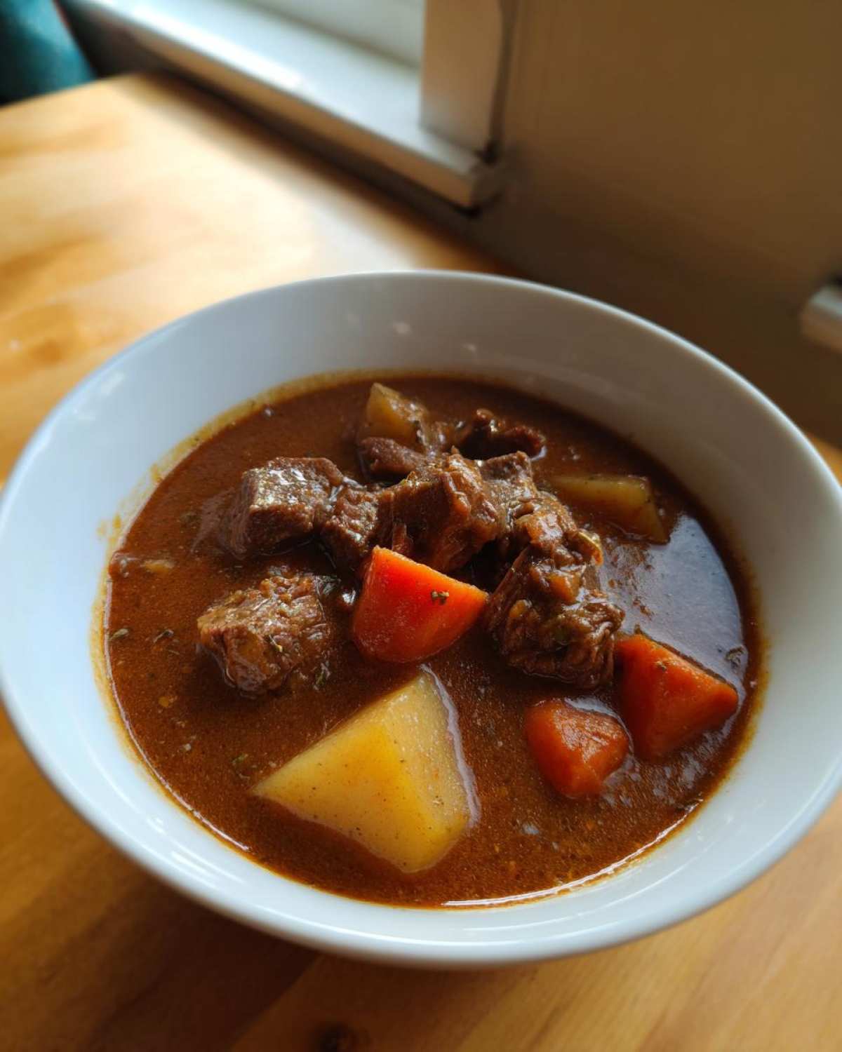 A close-up of a white bowl filled with rich, brown pork stew featuring chunks of meat, potatoes, and carrots.