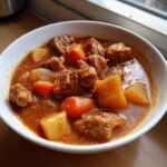 Close-up of a white bowl filled with rich, savory pork stew featuring tender chunks of meat, carrots, and potatoes.
