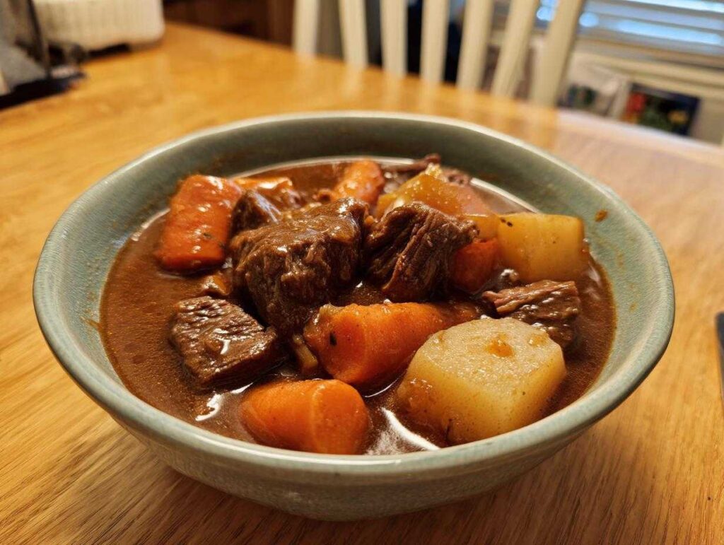Close-up of a rustic bowl filled with rich, dark pork stew featuring tender meat chunks, carrots, and potatoes.