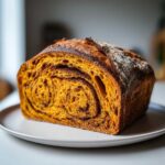 Cross-section of a vibrant orange pumpkin sourdough loaf showing a dark cinnamon swirl pattern.