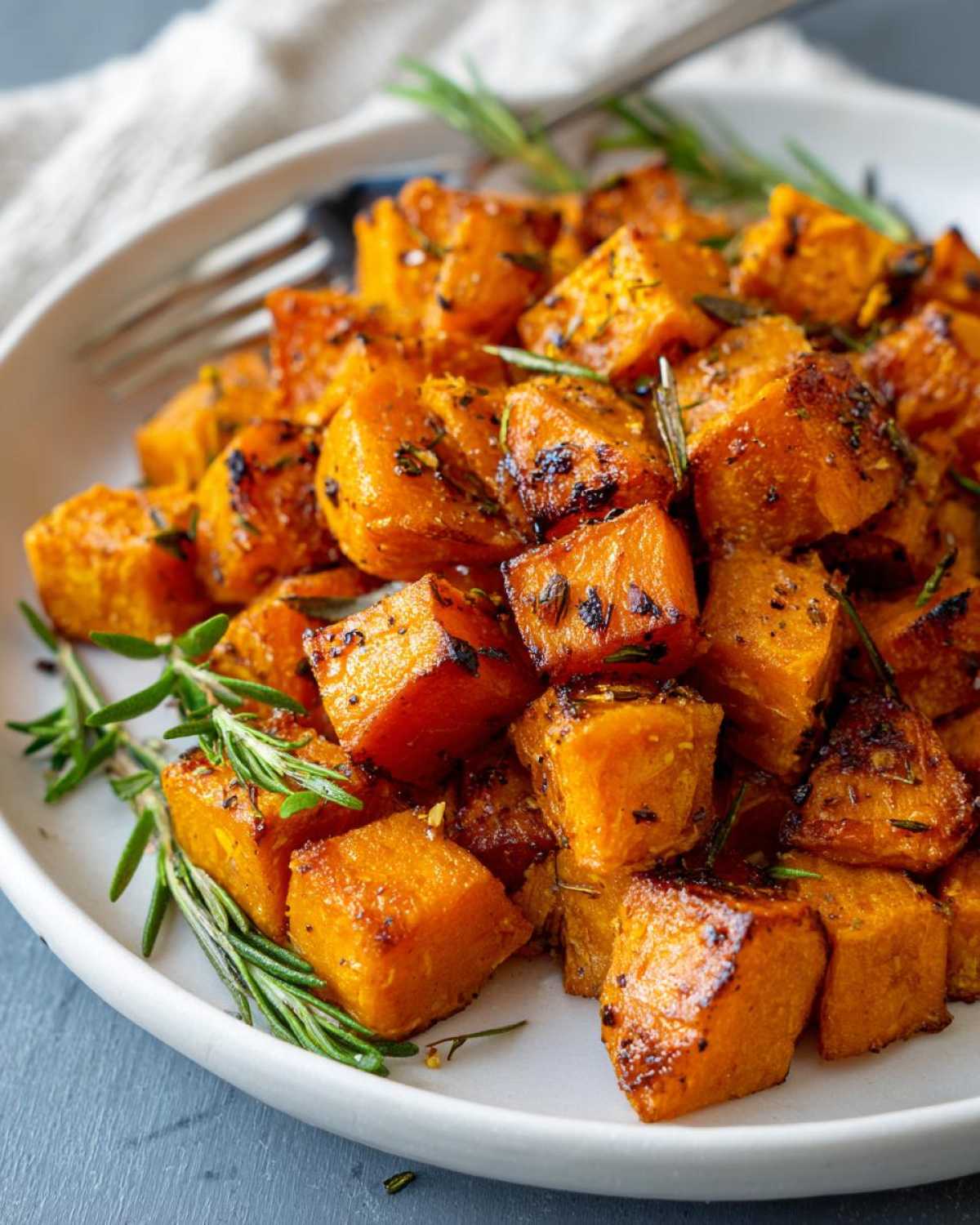 Close-up of caramelized roasted sweet potatoes cubes seasoned with herbs and fresh rosemary sprigs.