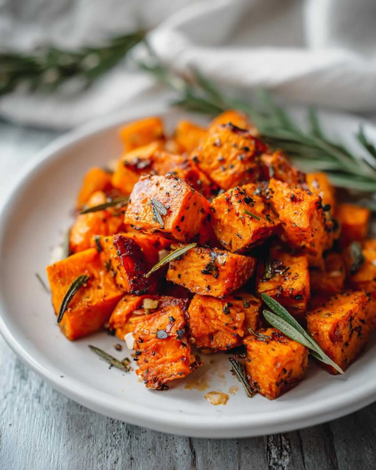 Close-up of perfectly seasoned roasted sweet potatoes cubes garnished with fresh rosemary sprigs.