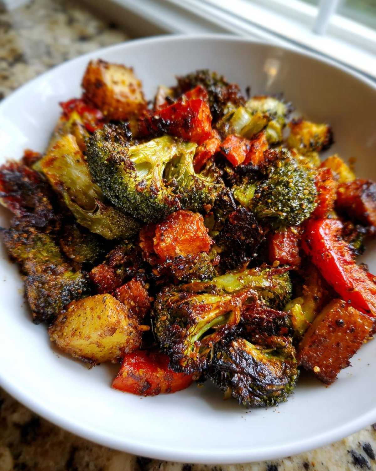 Close-up of perfectly seasoned and charred roasted vegetables, including broccoli and sweet potatoes, served in a white bowl.