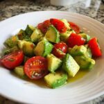 A close-up shot of a vibrant avocado salad featuring diced avocado and halved cherry tomatoes tossed in a light vinaigrette.